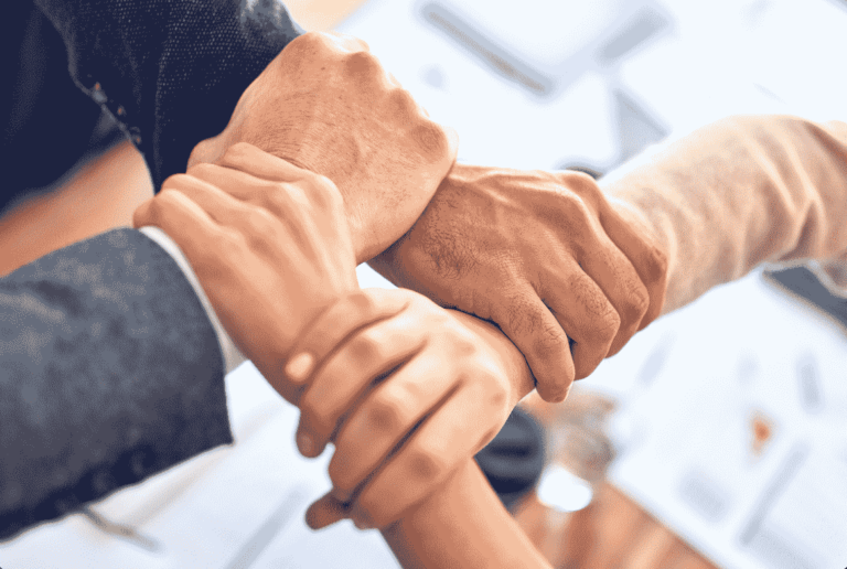 Four people joining hands showing teamwork and leadership